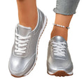 Silver sneakers with white laces worn by a person on a tiled floor.